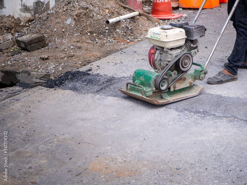 Worker use vibratory plate compactor compacting asphalt