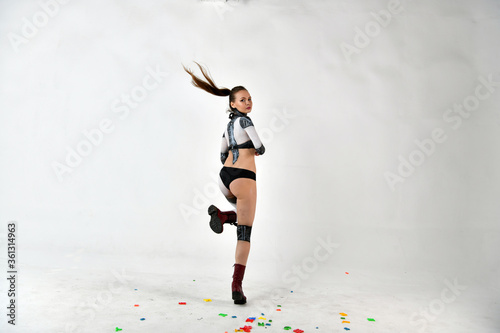 beautiful girl in a robot suit throws up multi-colored letters and does gymnastic exercises on a white background