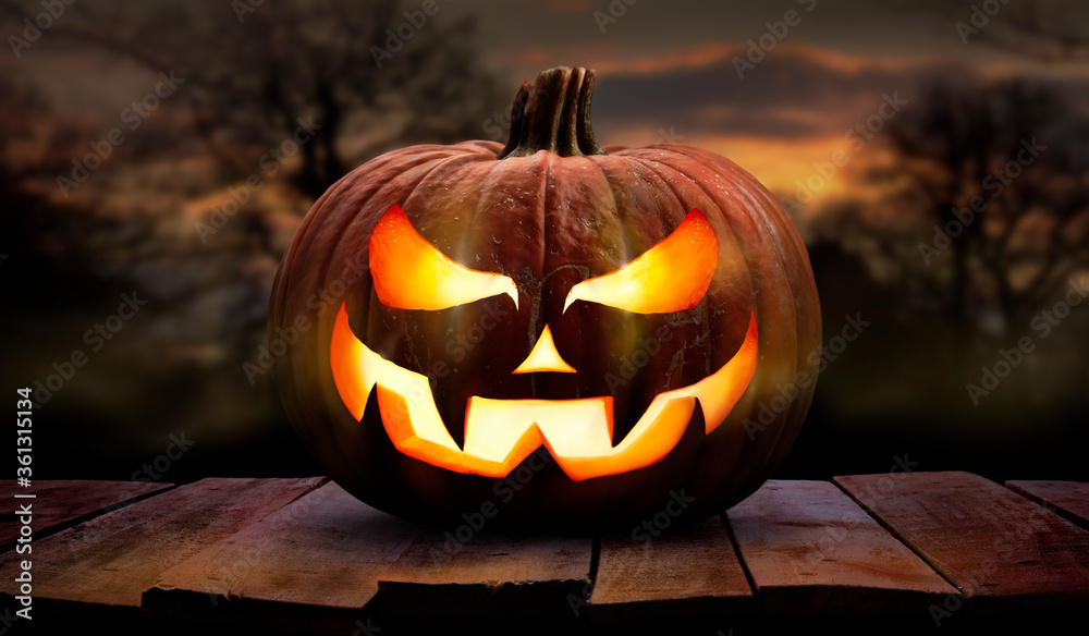 One spooky halloween pumpkin, Jack O Lantern, with an evil face and eyes on a wooden bench, table with a sunset, night background.