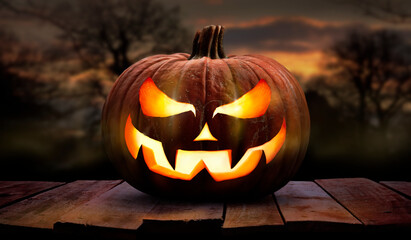 One spooky halloween pumpkin, Jack O Lantern, with an evil face and eyes on a wooden bench, table with a sunset, night background.