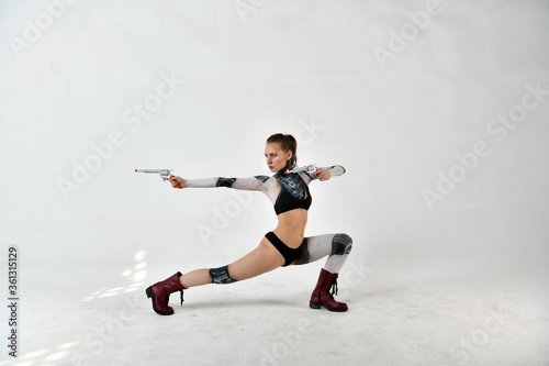 beautiful girl in a robot suit makes fighting movements with silver revolvers on a white background