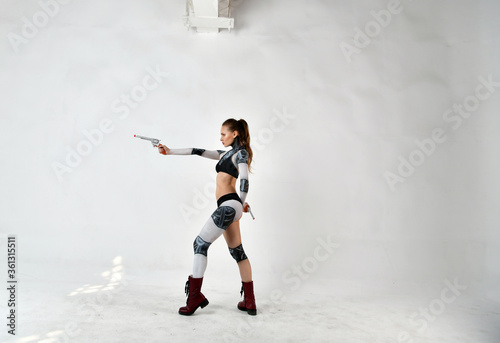 beautiful girl in a robot suit makes fighting movements with silver revolvers on a white background