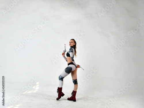 beautiful girl in a robot suit makes fighting movements with silver revolvers on a white background