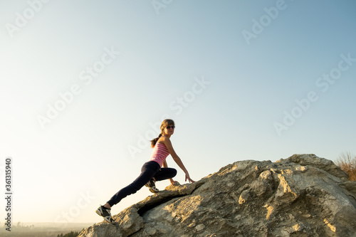 Woman hiker climbing steep big rock on a sunny day. Young female climber overcomes difficult climbing route. Active recreation in nature concept.