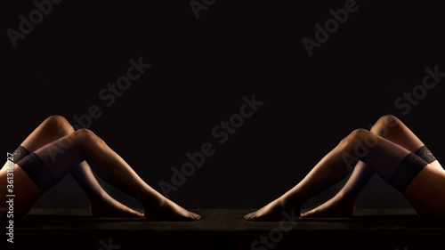 Legs of two women in black stockings in front of black background