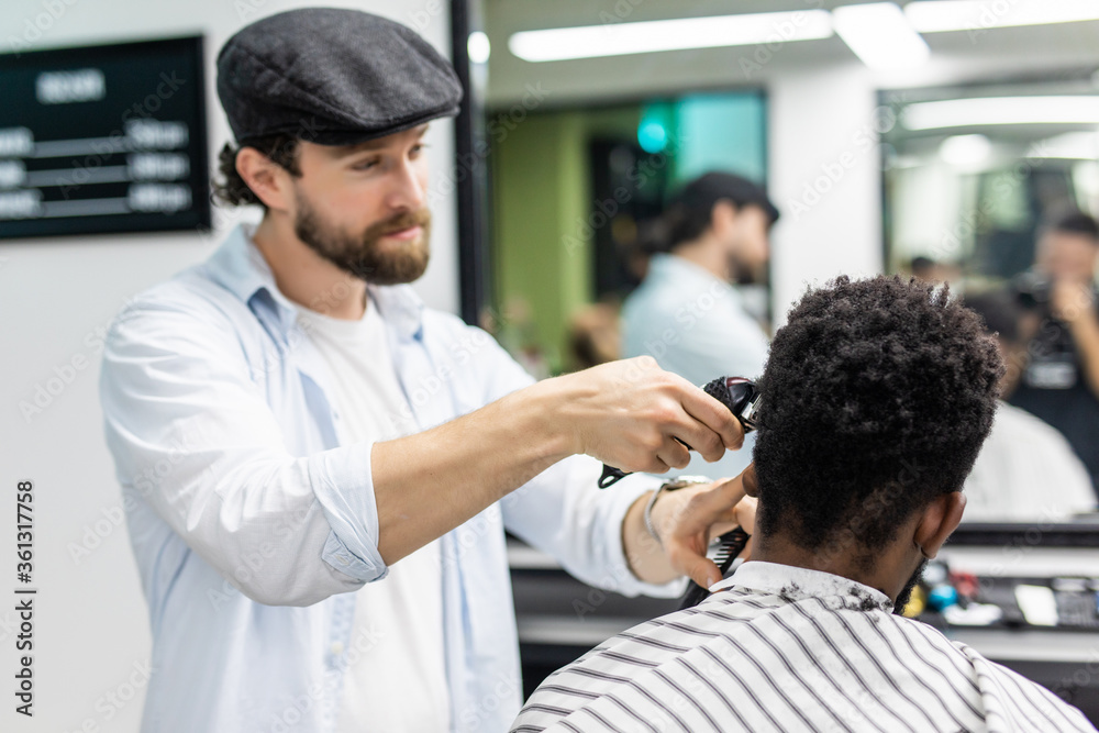 Fototapeta premium . Male beauty treatment concept. Smiling young African guy getting new haircut in barber salon. Portrait of barbers client