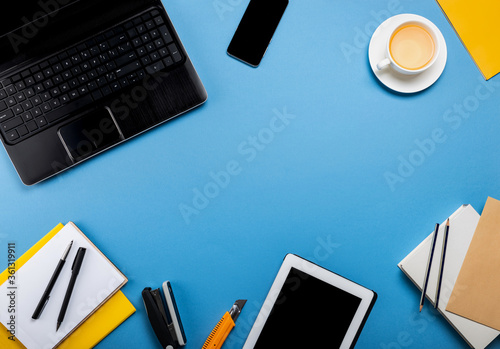 Online work or education concept. Laptop, tablet computer, smartphone, notepad, book, stationery on the blue background. Top view with copy space.