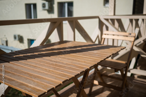 Wooden table with chairs stands on the balcony of the motel. Wooden table at a motel in sunny weather close-up.