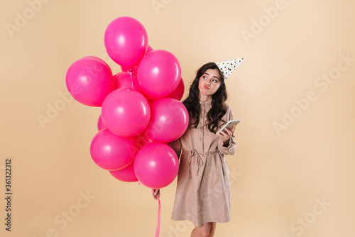 Image of confused woman using cellphone while posing with pink balloons