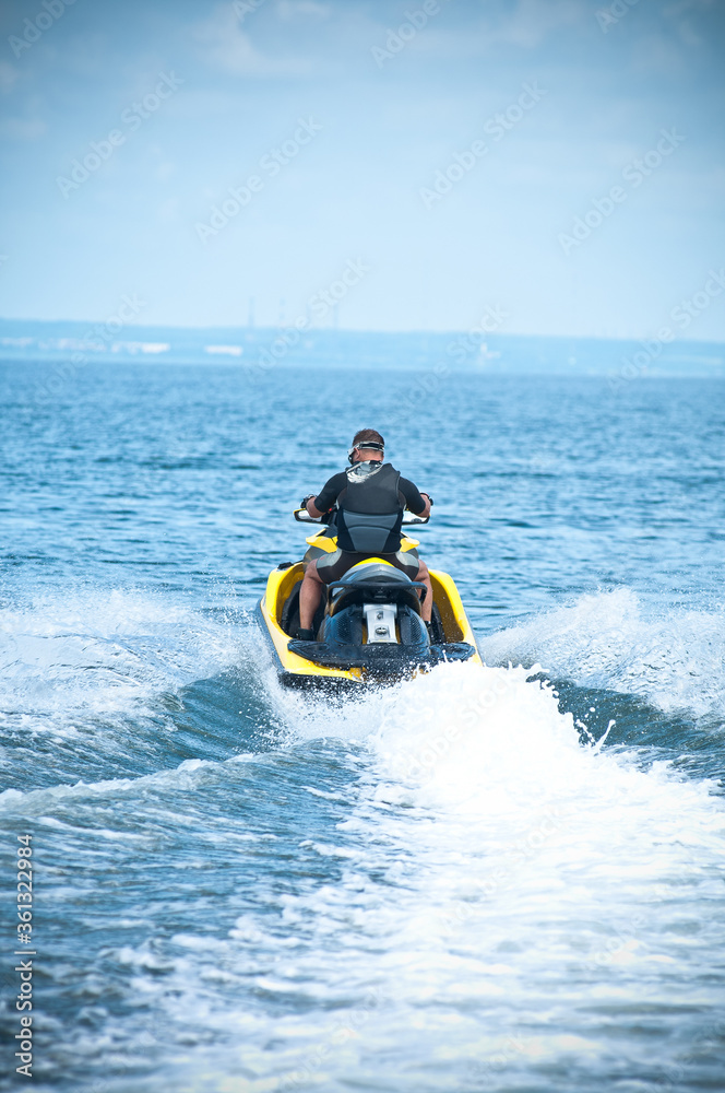 Man of jet ski rider performs on the waves with much splashes goes to sea