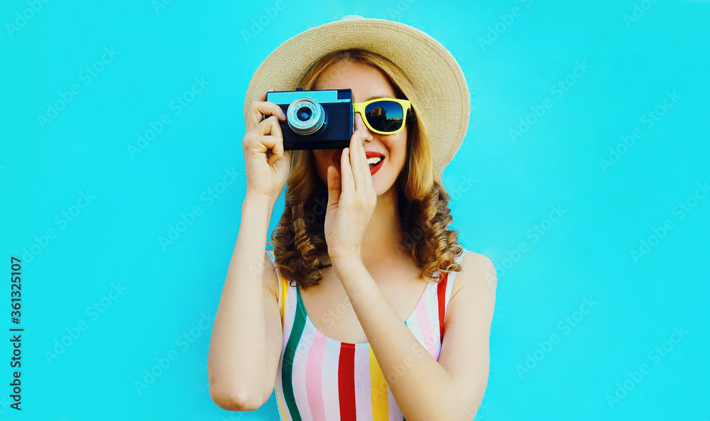 Summer portrait happy smiling young woman with retro camera wearing a summer straw hat on blue background