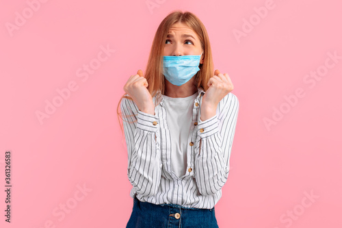young excited thoughtful woman in a medical protective mask on her face makes a wish on a pink background