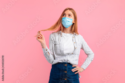 pensive young woman in a medical protective mask on her face, on an isolated pink background. Coronavirus epidemic, quarantine, virus protection