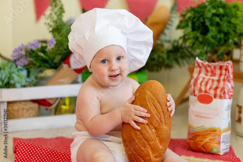 portrait of a baby in a cook's hat with bread in his hands in a beautiful photo zone with flour and vegetables, a cook's child, a child eating bread, preparing food