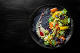 Fresh summer vegetarian salad, cucumber slices, carrot, avocado, orange and salad mix in plate on black wooden table background