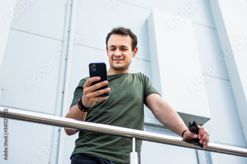Young successful man pensive typing on his cellphone on building background