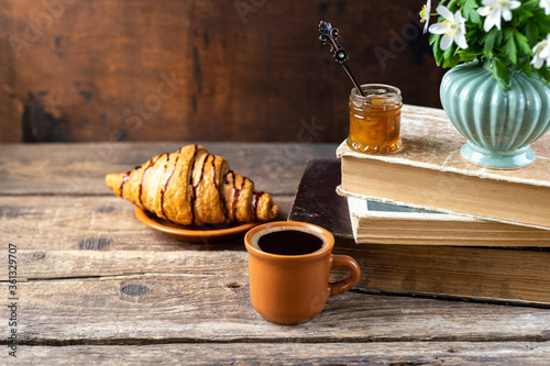 Bouquets of forest flowers, coffee cup, old books, croissants on wooden rustic table. Good morning, breakfast, reading, cozy home, hygge concept. Copy space