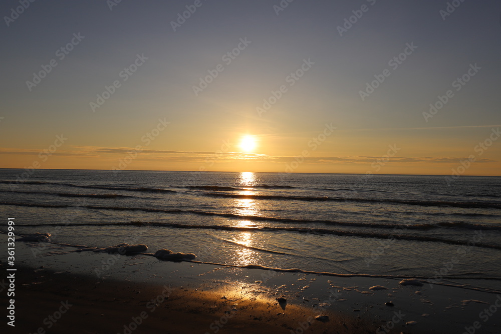 Beautiful warm golden sunlit clouds during sunset perfectly reflecting in the sand on a beach.