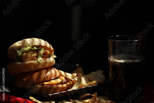  Burger lezat dengan saus pedas di piring dengan tikar serbet merah, keripik kentang dan minuman cola di ruangan gelap. Fotografi makanan komersial