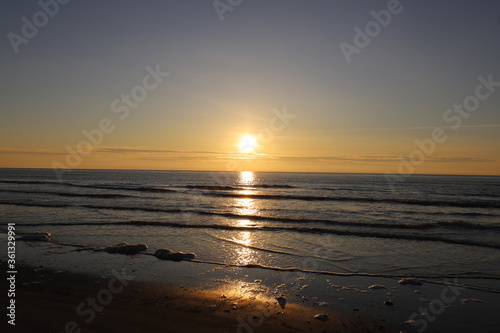 Beautiful warm golden sunlit clouds during sunset perfectly reflecting in the sand on a beach.