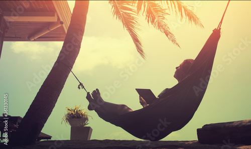 Woman an using a digital tablet  while relaxing in a hammock on a sand tropical summer beach photo