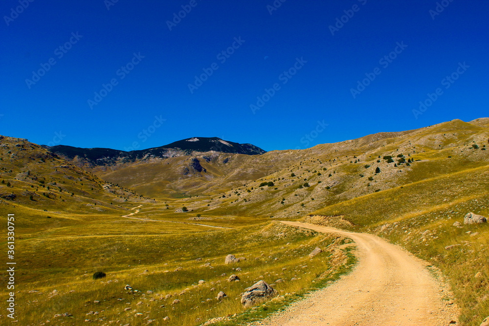 Oversaturated. Old mountain road, rocky landscape, mountain top in the background with blue sky and moon. Bjelasnica Mountain, Bosnia and Herzegovina.