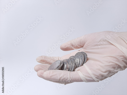 A hand in white latex glove holds money, Indonesian coins. Isolated in white background. Side view.