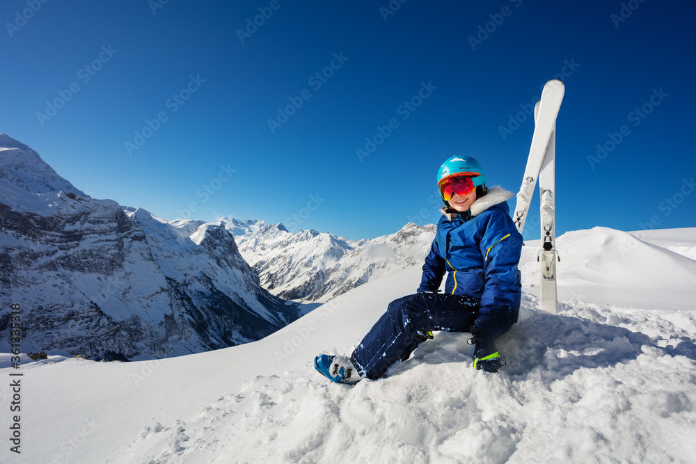 Portrait in the mountains of a girl in blue helmet and ski outfit over the sky sit in snow on alpine resort Portrait in the mountains of a girl in blue helmet and ski outfit over the sky sit in snow on alpine resort
