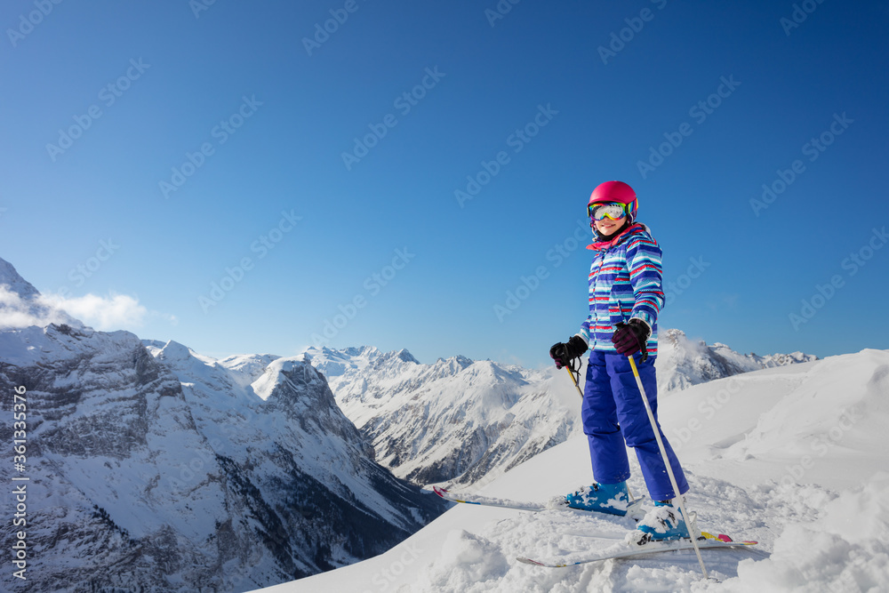 Portrait of a ski girl stand in colorful vivid sport clothes, helmet and glasses over Alps mountain tops view