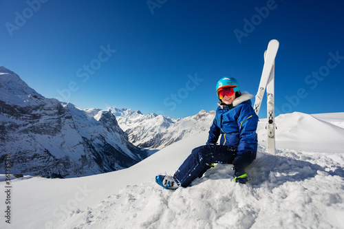 Portrait in the mountains of a girl in blue helmet and ski outfit over the sky sit in snow on alpine resort