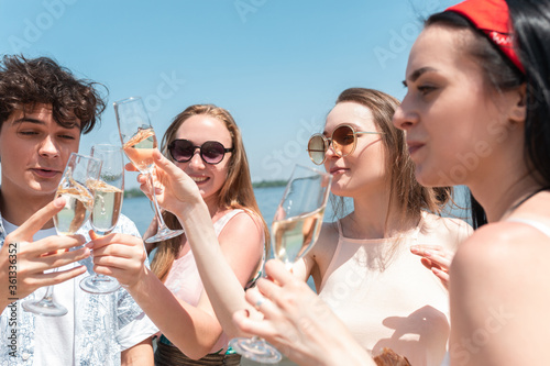Close up clinking, cheers. Seasonal feast at beach resort. Group of friends celebrating, resting, having fun in sunny summer day. Look happy and cheerful. Festive time, wellness, holiday, party.
