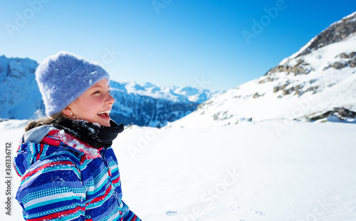 Happy laughing with open mouth girl in ski hat and color coat high in snow covered mountains view in profile