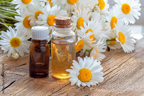 Bottles of essential oil and chamomile flowers on wooden table. Essential oil in a glass bottle with fresh chamomile flowers, beauty treatments. Spa concept.