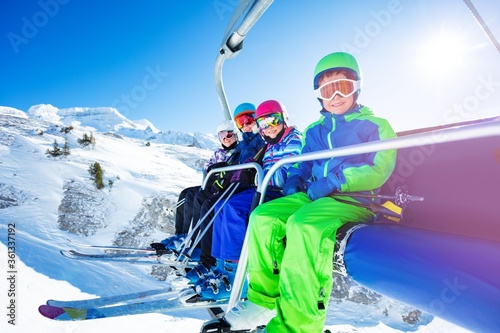 Portrait of four happy kids in vivid ski outfit lifting on chairlift on the mountain together and smiling