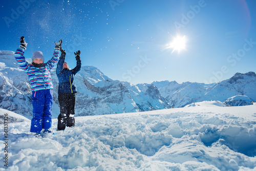 Two cute girls have fun stand together throw snow in the air over beautiful mountain view