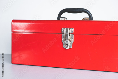 closed red tool box with a black handle on a gray background, highlight on the left. place for an inscription. lock.