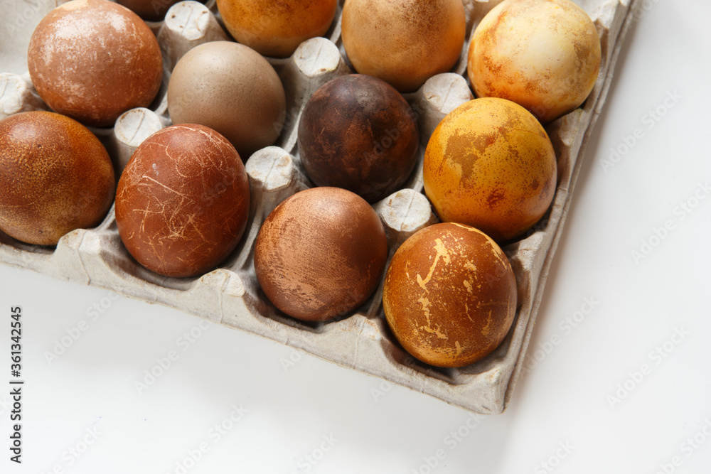 top view shot of a box of twelve original, unique colorful dragon or dinosaur looking like chicken Easter eggs, dyed with natural products (red wine, tea, coffee, carrots, turmeric, soy sauce)