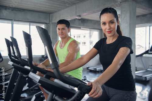 Select focus on Attractive Caucasian woman cycling on bike machine in gym fitness sport complex with handsome guy in background