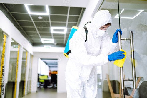 Cleaning and disinfection of office to prevent COVID-19. A disinfector man in a protective suit and mask washes office furniture disinfectants. Prevention of spreading pneumonia virus with surfaces.