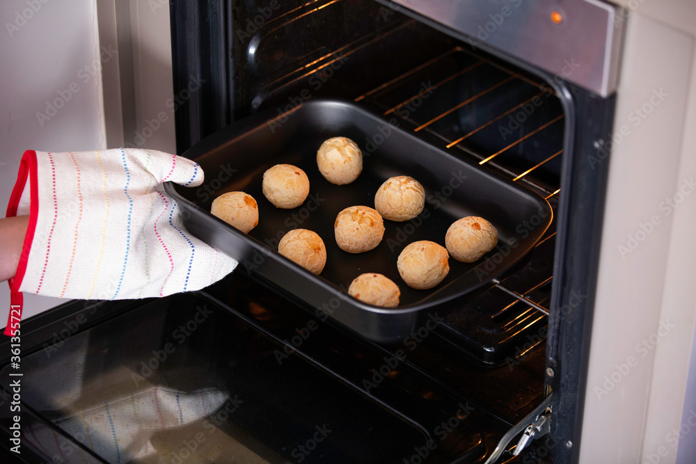 Woman hand with pot catching metal baking sheet with cheese bread from oven. Cheese buns.
