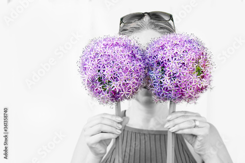 Portrait of women holding two big Allium instead of glasses in front of her face. Black and whtite photo with purple colored flowers. Monocotyledonous flowering plants. photo