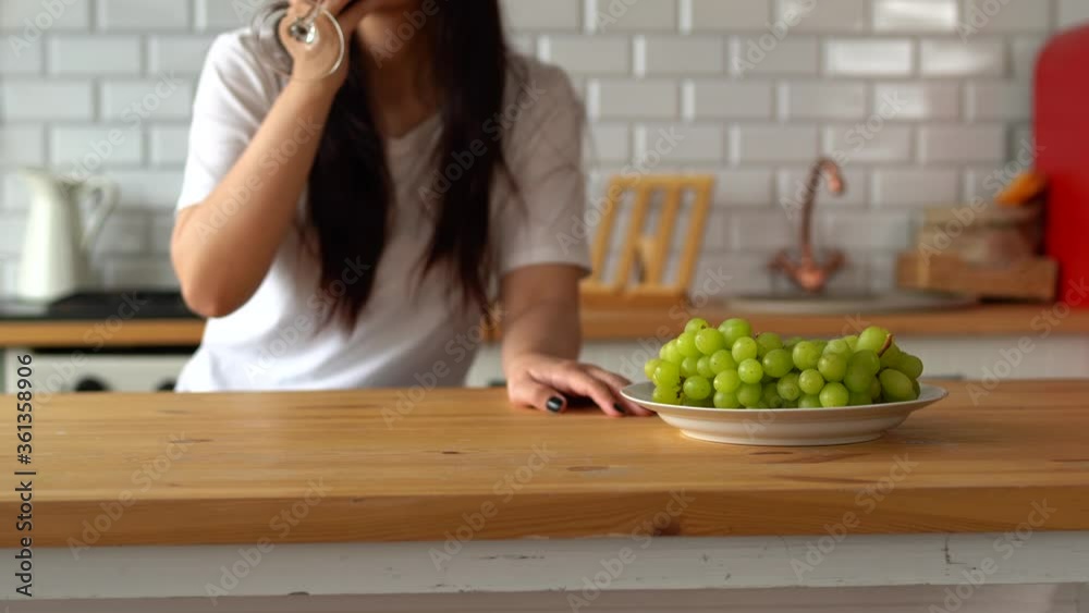 Young woman drinking red wine at table. Close up of adult female takes glass of wine, sitting in kitchen. Young woman drinking red wine at table. Close up of adult female takes glass of wine, sitting in kitchen.