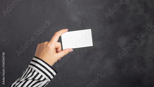 Female hand holds mockup business card, credit card, discount card on dark black background. Template for design.