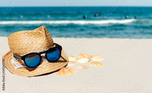 Vintage summer wicker straw beach hat and sunglasses on the beach near the sea.