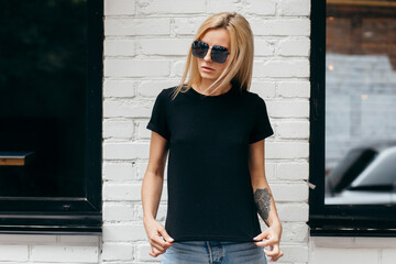Stylish blonde girl wearing black t-shirt and glasses posing against street , urban clothing style. Street photography