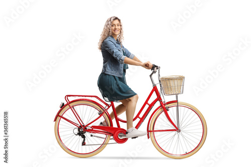 Side shot of a young woman in a dress riding a red bicycle and looking at the camera © Ljupco Smokovski
