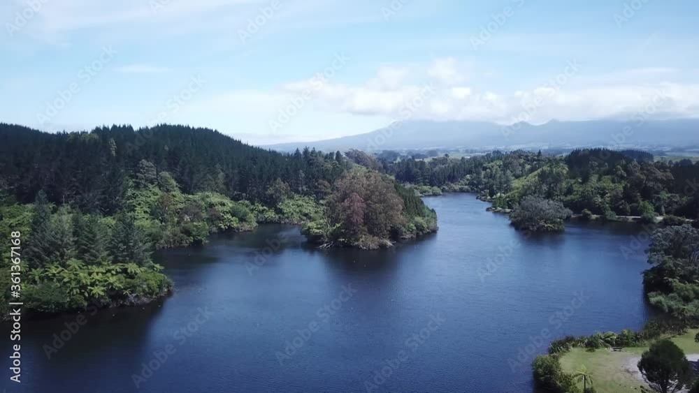 Drone shot, flying over lake towards forest with Mount Taranaki at the back, in New Plymouth, New Zealand. Drone shot, flying over lake towards forest with Mount Taranaki at the back, in New Plymouth, New Zealand.