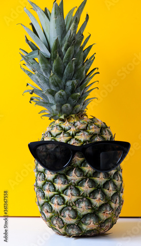 crazy pineapple with sunglasses in front of a yellow background, concept for summer or vacation
