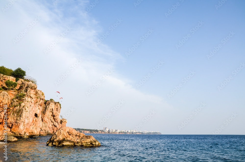 A men are flying on a paraglider over the Mediterranean sea coast and beach in the background of the panorama of the Turkish city of Antalya