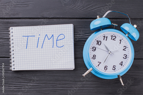 Alarm clock and notepad on dark wooden table. Time concept flat lay.